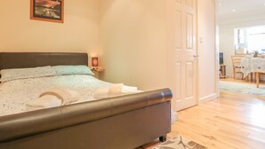 Un dormitorio con cama, mesita de noche, lámpara y una puerta que da a un comedor.