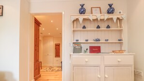 Un pasillo con suelo de madera, un armario blanco con cajones y una estantería con jarrones decorativos.