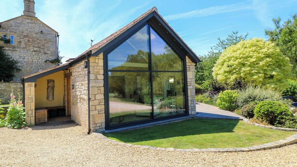 A modern house with a stone exterior and large glass windows. - Pheasant Cottage (Bath)