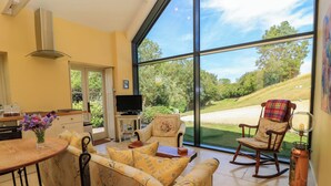 A spacious living area with a large window, a sofa, a chair, and a television. - Pheasant Cottage (Bath)