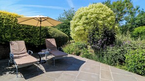 An outdoor patio with two lounge chairs, a table, and a large umbrella. - Pheasant Cottage (Bath)