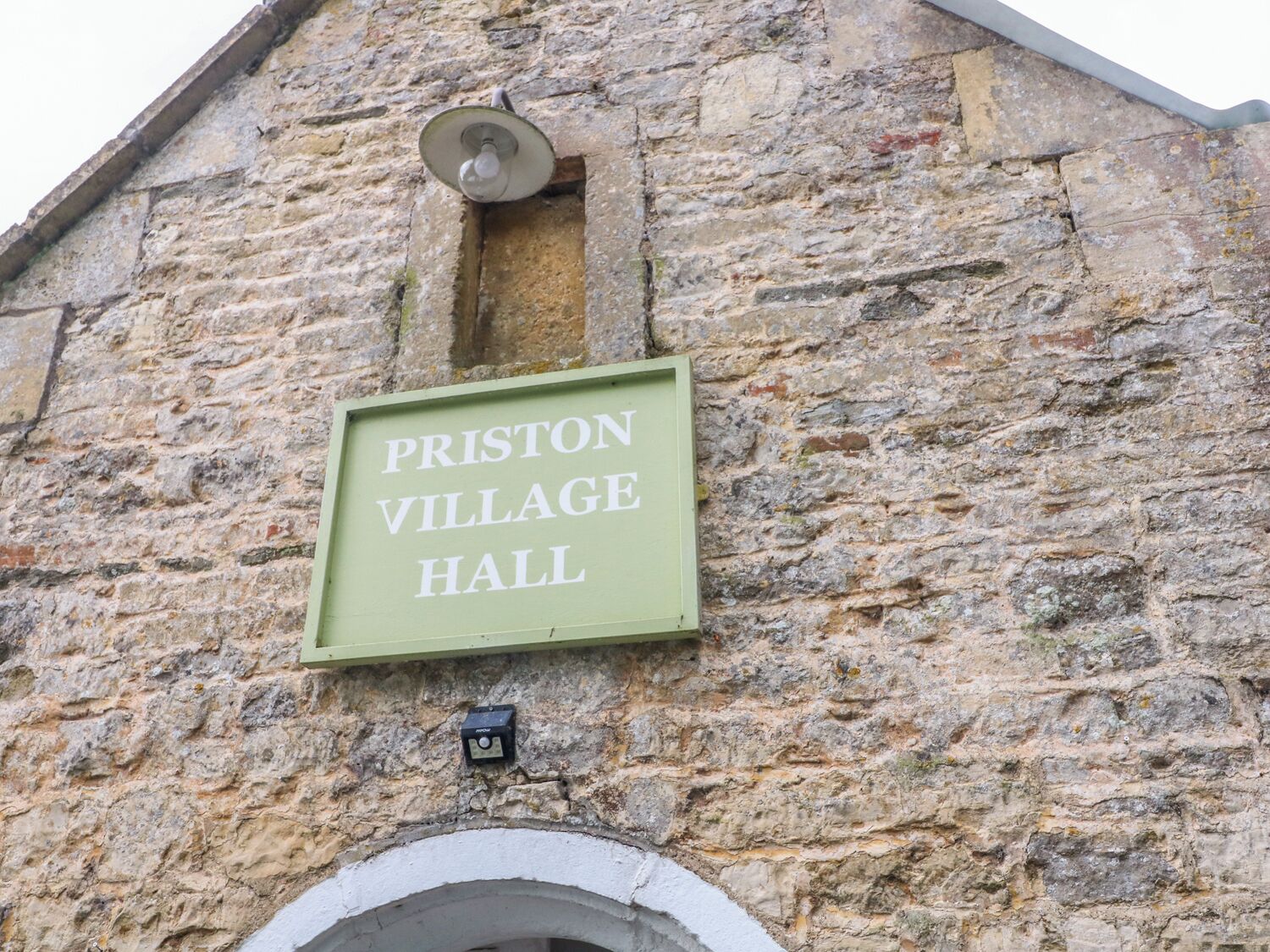 A sign for Priston Village Hall mounted on a stone wall.