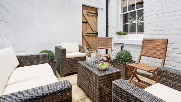 A patio area with wicker furniture, a wooden door, and a white brick wall.