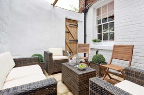 A patio area with wicker furniture, a wooden door, and a white brick wall. - Harbour House (Whitby)