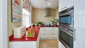 A kitchen with white cabinets, a red countertop, a bread box, a sink, and a stainless steel oven.