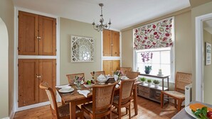A dining area with wooden furniture, a chandelier, and a window with a floral blind.