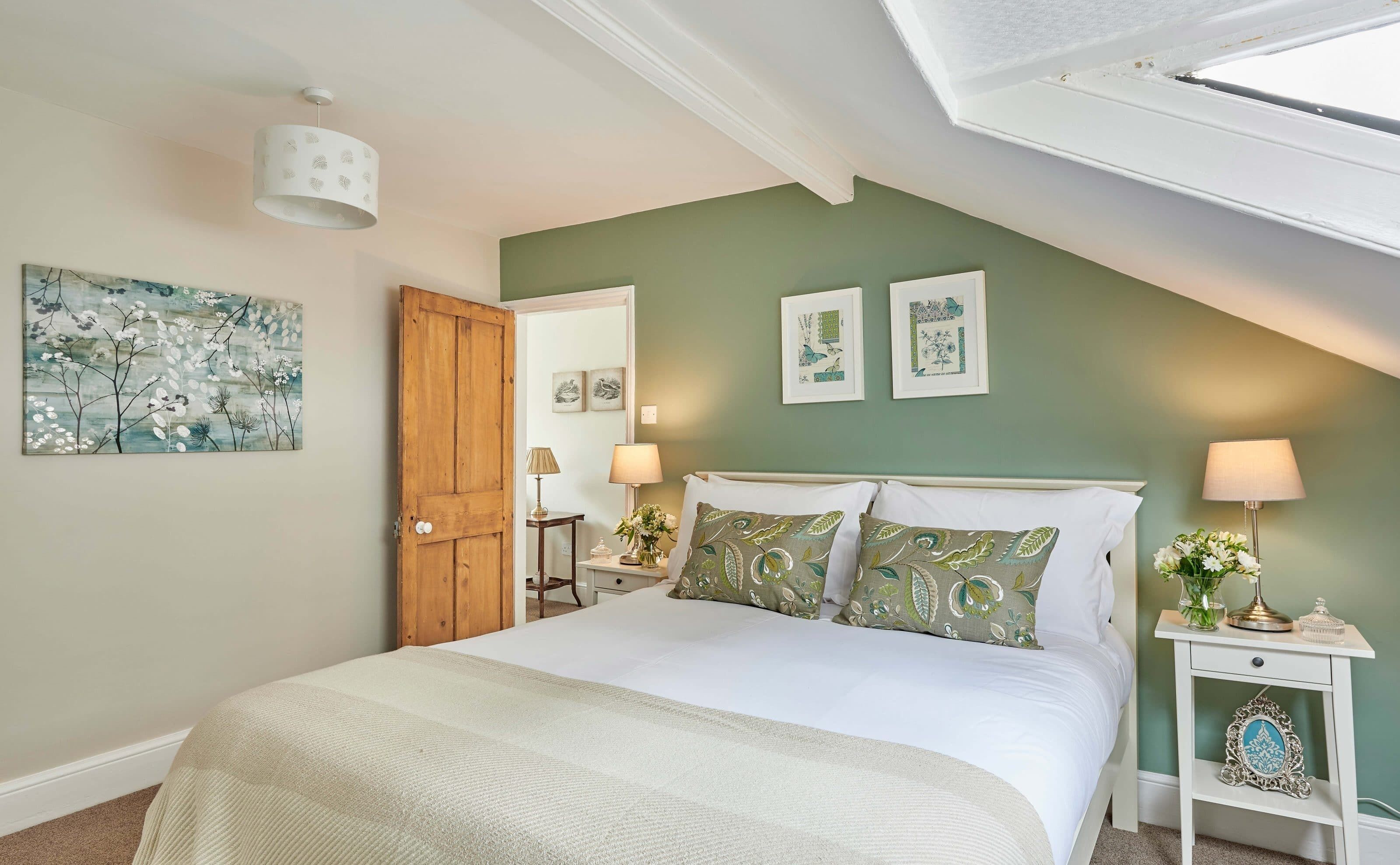 A bedroom with a bed, a nightstand, a lamp, a door, and wall art.