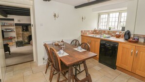 Uma cozinha com armários de madeira, uma mesa de jantar com cadeiras, forno embutido e uma janela.