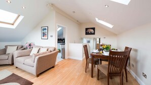 Ein modernes Wohnzimmer mit hohen Decken, Dachfenstern, einem Essbereich mit Holzmöbeln und einer Küche im Hintergrund.