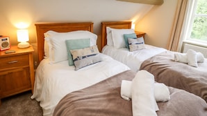 Une chambre avec deux lits, une table de chevet avec une lampe et une fenêtre avec des rideaux.