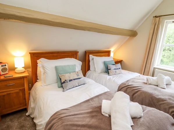 A bedroom with two beds, a bedside table with a lamp, and a window with curtains.