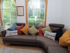Un sofá modular con varios cojines de distintos colores, ubicado frente a un amplio ventanal con vistas a zonas verdes.