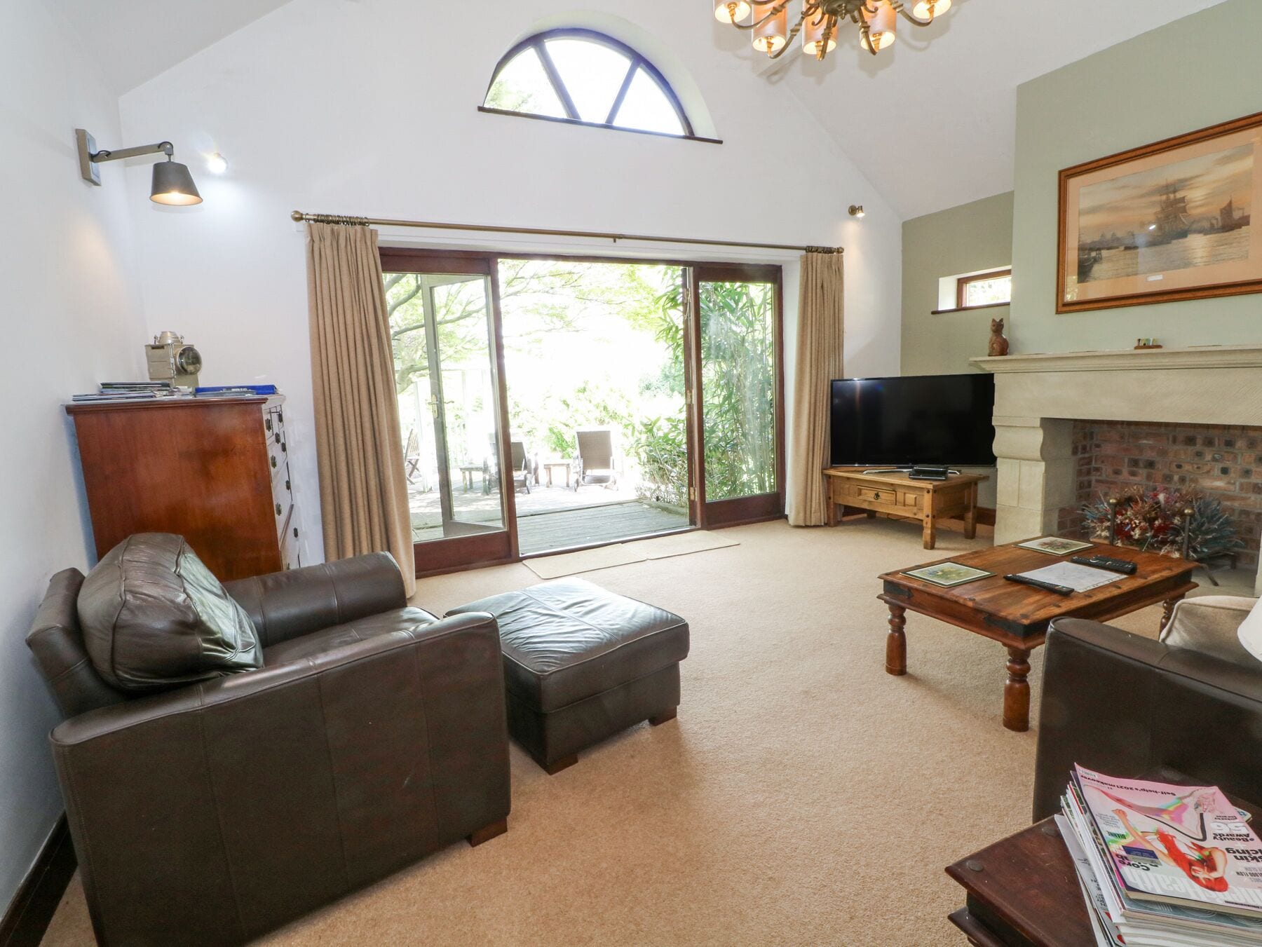 A spacious living room with a large sliding glass door leading to a balcony, a fireplace, a television, and a coffee table.
