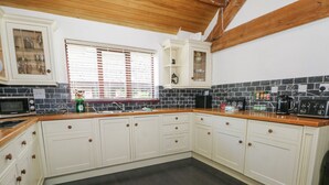 A kitchen with white cabinets, a black tiled backsplash, a wooden countertop, and a window with blinds. - Frog Meadow Barn (Stoke-on-Trent)