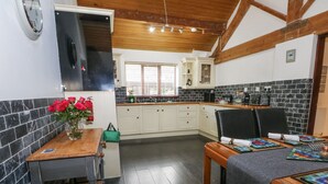 A compact kitchen with white cabinets, a wooden table, and a dining area with a table set for two. - Frog Meadow Barn (Stoke-on-Trent)