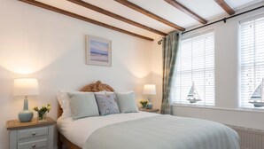 Quarto com cama, mesas de cabeceira, luminárias, uma janela com cortinas e um quadro na parede.