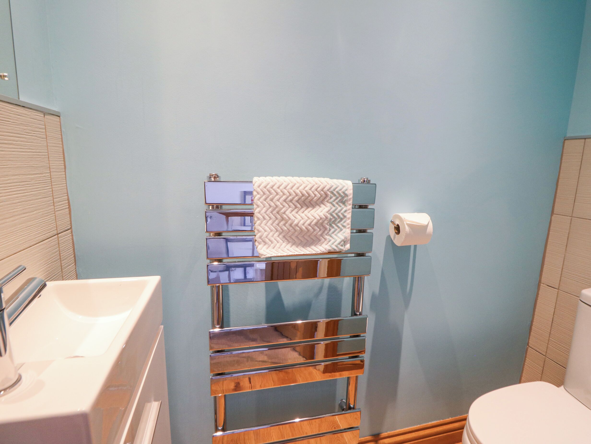 A bathroom with a white sink, a mirror, a towel rack with a towel, and a toilet.
