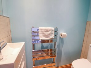A bathroom with a white sink, a mirror, a towel rack with a towel, and a toilet.