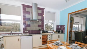 A modern kitchen with a built-in dishwasher, a large window, and a dining area set for four. - Ty'r Orsaf (Builth Wells)