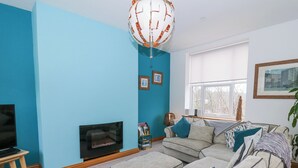 A living room with a sofa, a television, a fireplace, and a window with a view of trees. - Ty'r Orsaf (Builth Wells)