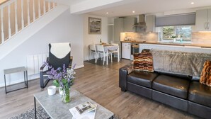 A modern living room with a sofa, coffee table, and a dining area with chairs and a table. - Cuckoo Cottage (Bridport)