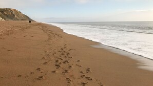 A sandy beach with footprints leading to the water, a cliff in the background, and a clear sky. - Cuckoo Cottage (Bridport)