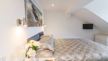 A bedroom with a bed, a bedside table with a vase of flowers, a painting on the wall, and a television on the ceiling.