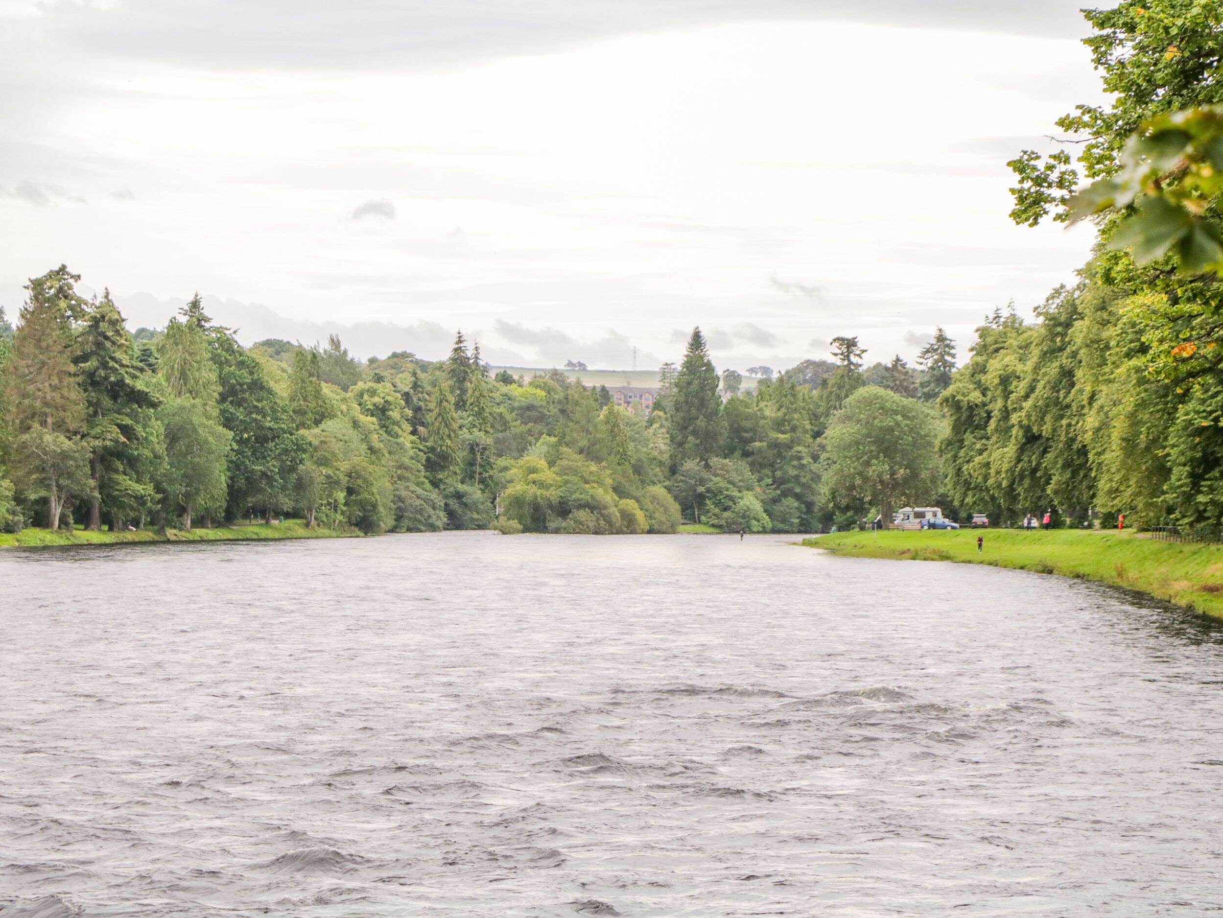 A river with a forested area on both sides and a distant building.