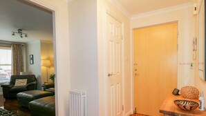 A room with a wooden floor, a radiator, a wooden door, a small table with a decorative bowl, and a chair. - 7 Riverside Gardens (Inverness)