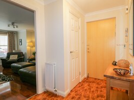 Una habitación con piso de madera, un radiador, una puerta de madera, una mesa pequeña con un cuenco decorativo y una silla.
