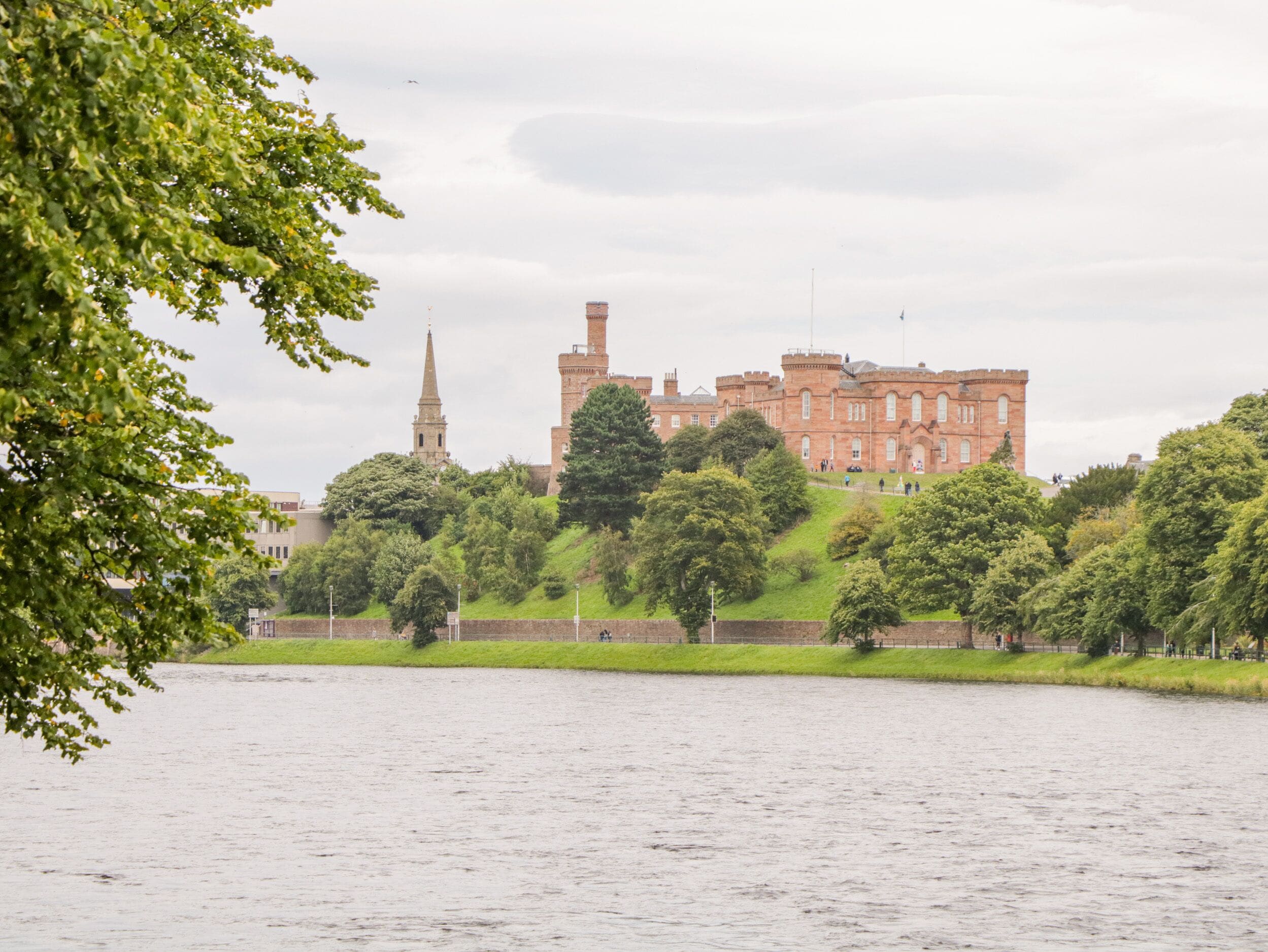 A historic building with a prominent tower, surrounded by lush greenery and a body of water.