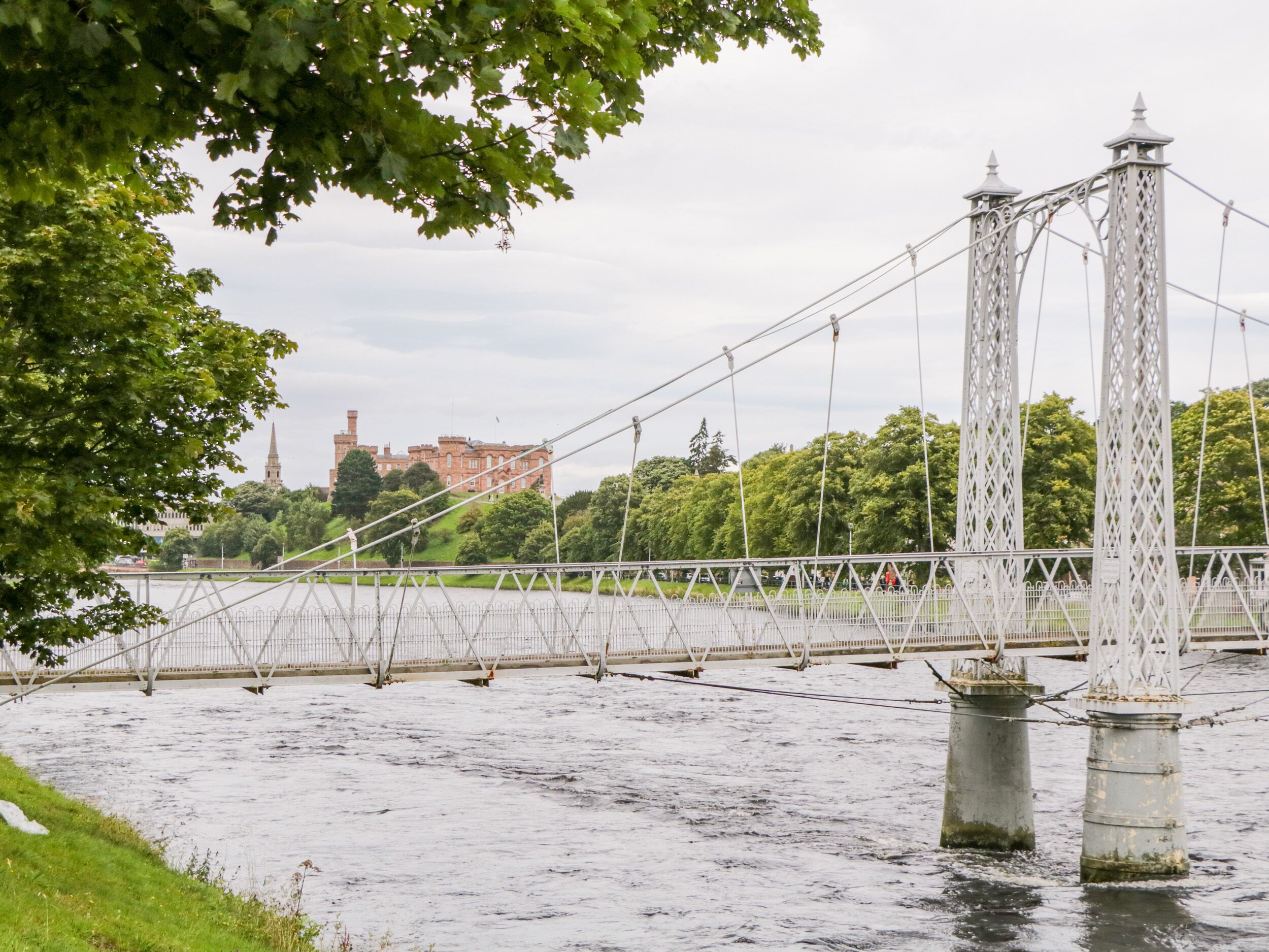 Un pont suspendu enjambant une rivière, avec un château en arrière-plan.