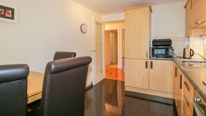 A compact kitchen with a dining area, a microwave, a kettle, and a clock on the wall. - 7 Riverside Gardens (Inverness)