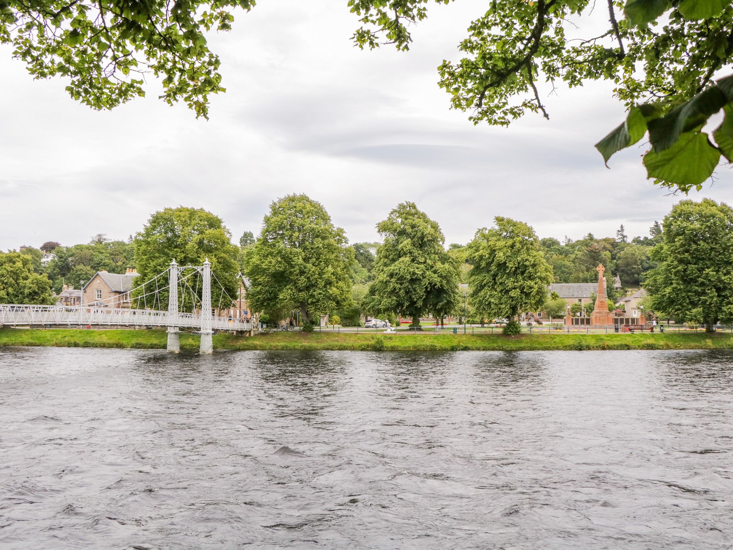 A riverside view with a bridge, trees, and a building with a tower.