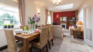 A dining area with a wooden table, wicker chairs, and a view of the garden through large windows. - Mews Cottage (Whitby)