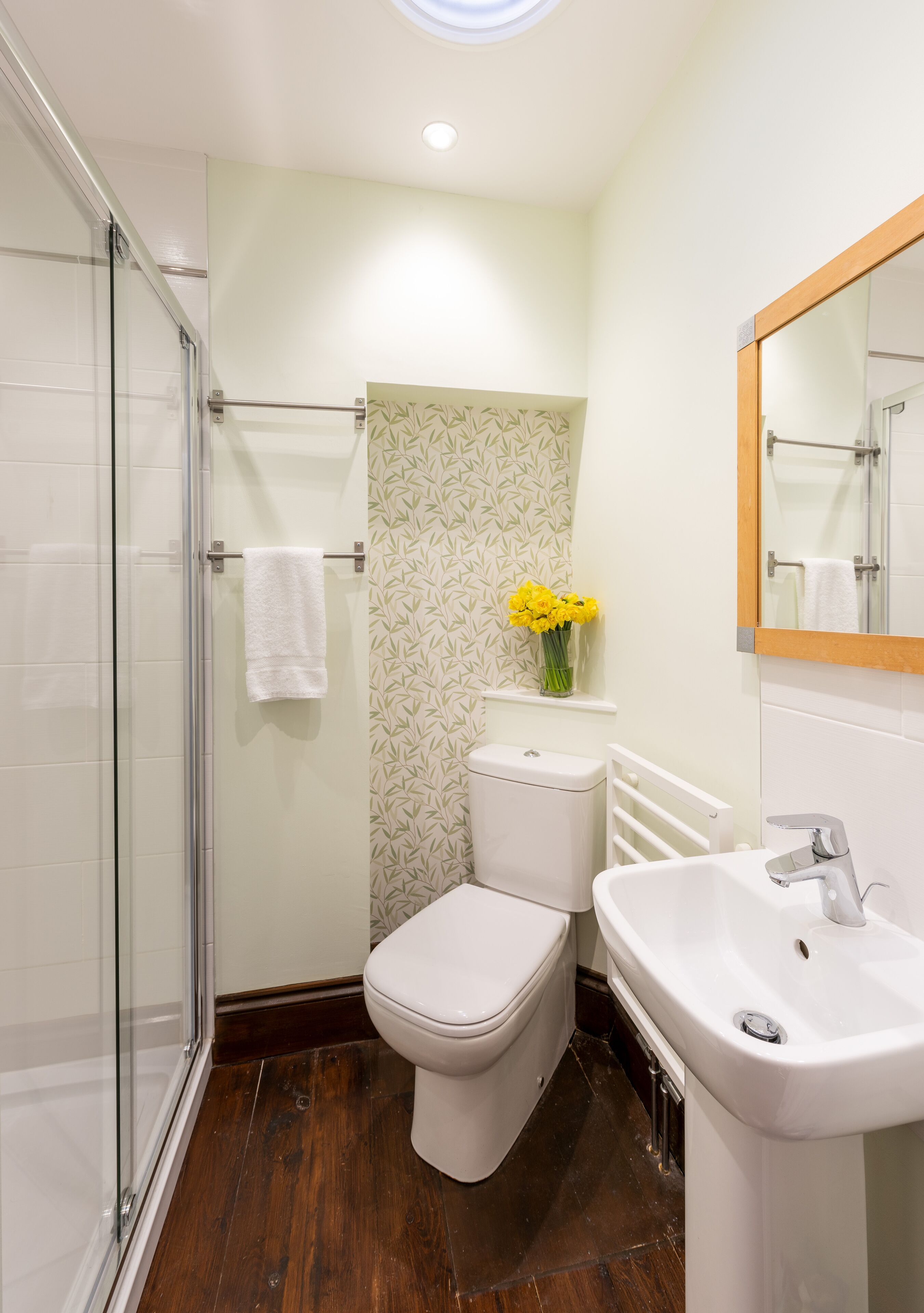 A bathroom with a glass shower enclosure, a toilet, a sink, and a mirror.