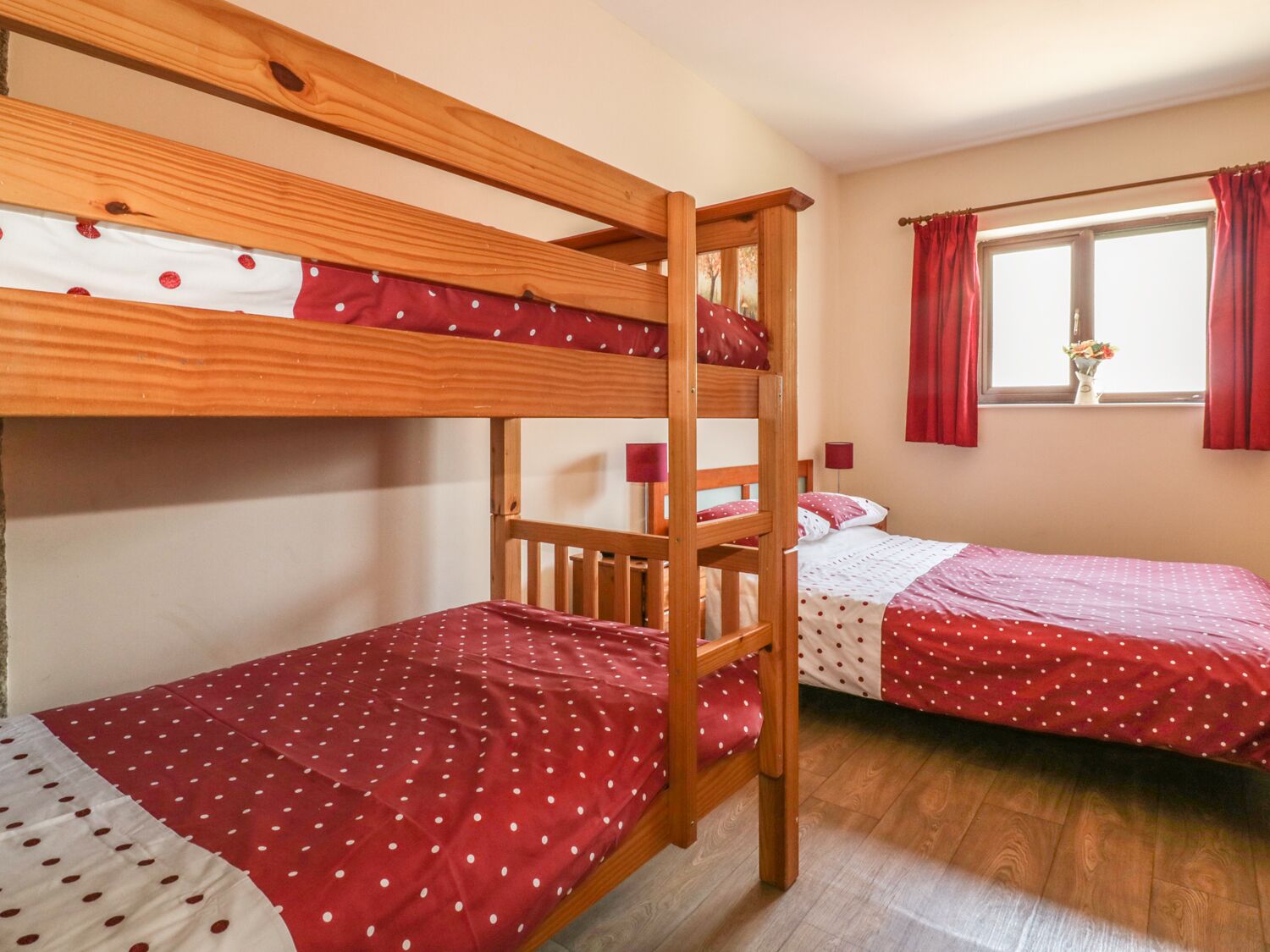 A room with two bunk beds, each with a red polka dot bedspread, and a window with red curtains.