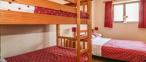 A room with two bunk beds, each with a red polka dot bedspread, and a window with red curtains.