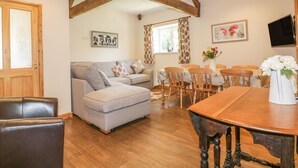 A cozy living room with a sofa, a dining table with chairs, wooden beams on the ceiling, and artwork on the walls.