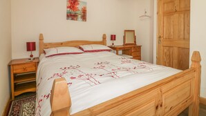 A wooden bed with a white and red floral bedspread, two bedside tables with lamps, a wooden wardrobe, and a painting on the wall.