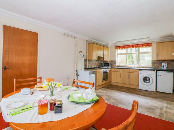 Cocina compacta con comedor. Incluye estufa, microondas, horno, lavadora y un lavamanos. La mesa del comedor está servida con platos, tazas y un jarrón de flores.