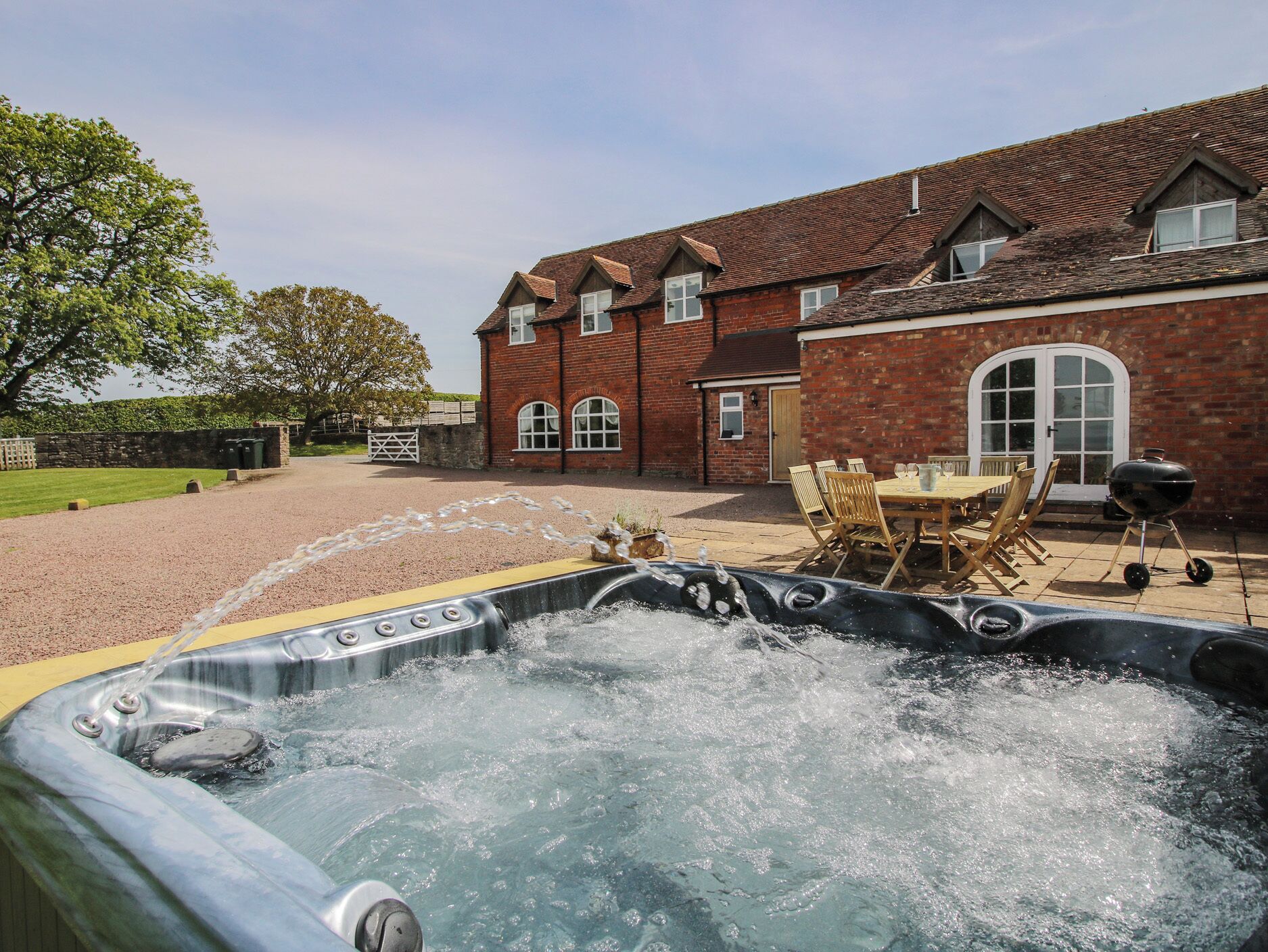 A hot tub in a backyard with a brick house and a dining table.