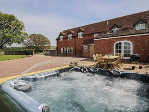 A hot tub in a backyard with a brick house and a dining table.