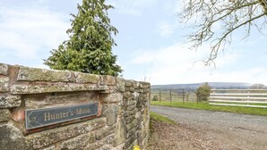 Un mur de pierres sur lequel est apposée une pancarte indiquant « Hunter’s Moon », et une vue sur un paysage rural avec une clôture et un arbre.