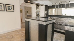 A modern kitchen with a black and silver bar counter, a large mirror, and framed pictures on the wall. - Maes Elwy (Saint Asaph)