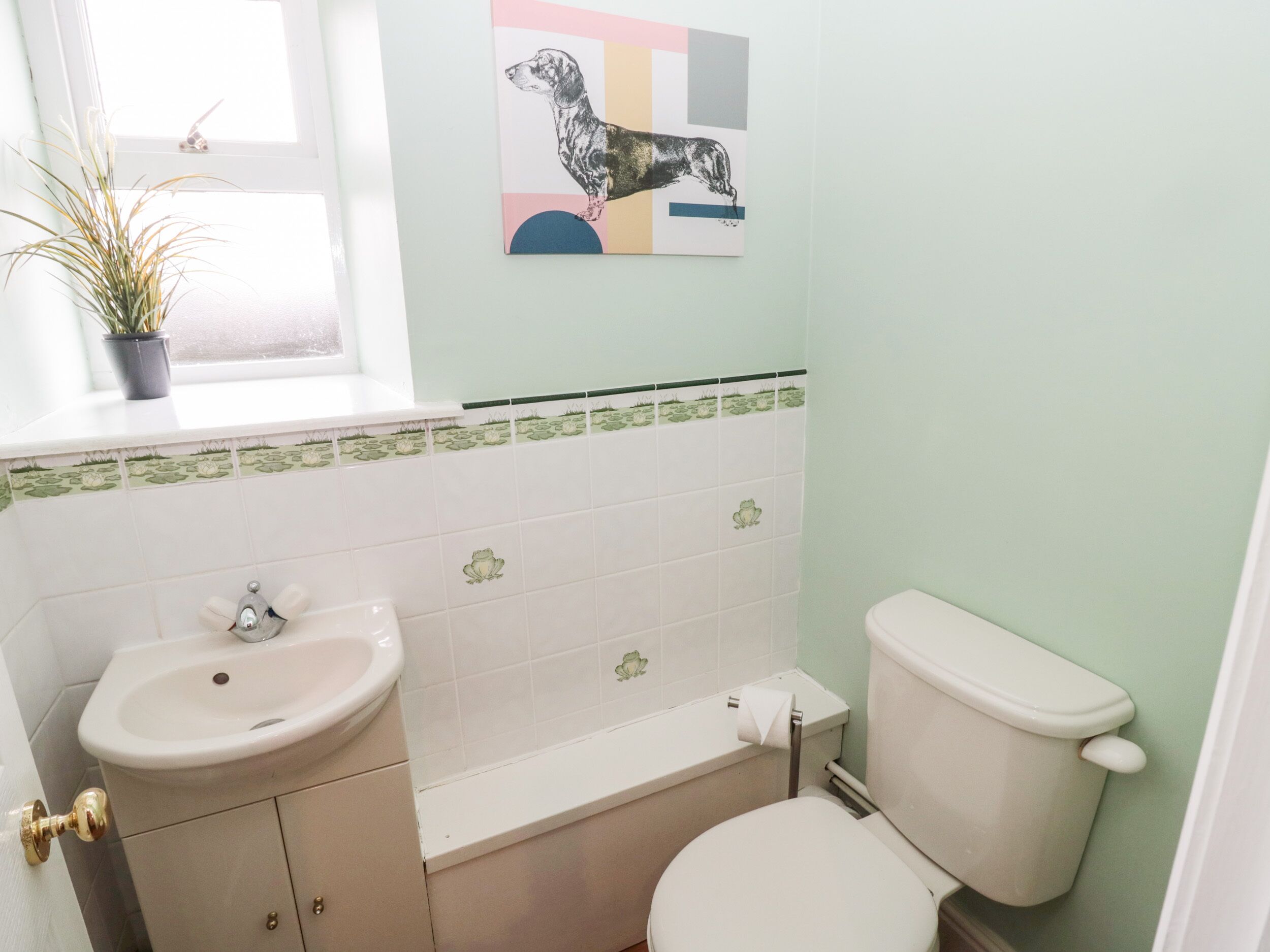 A bathroom with a sink, toilet, and a window with a plant.