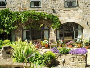 A stone building with a garden in front, featuring a wooden bench and potted plants. - The Steadings (Morpeth)