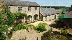 A stone building with a courtyard, a small pond, and outdoor seating. - The Steadings (Morpeth)