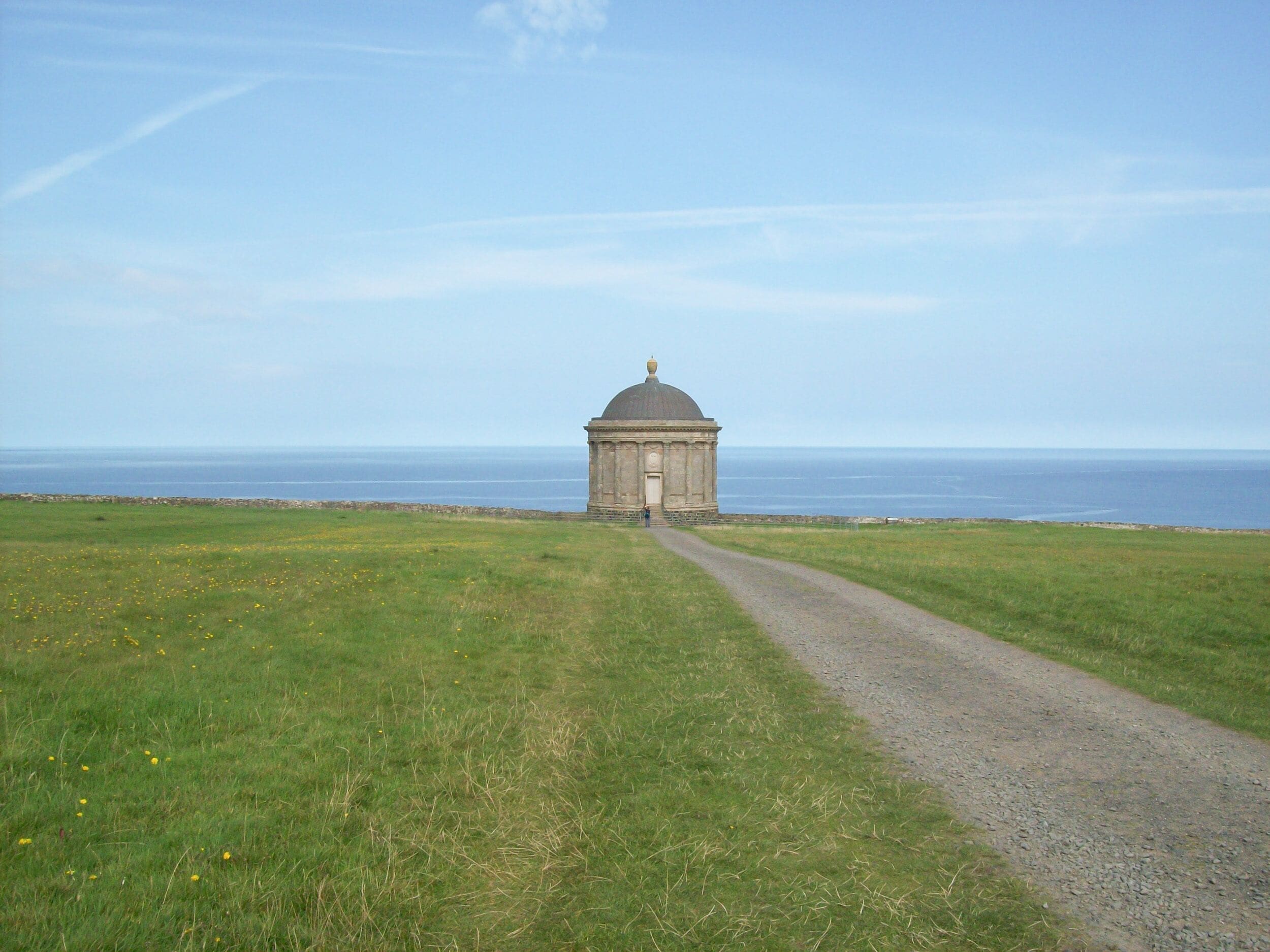 A solitary building with a dome, a gravel path leading to it, and a grassy field in the foreground.