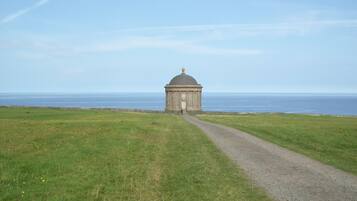 A solitary building with a dome, a gravel path leading to it, and a grassy field in the foreground.